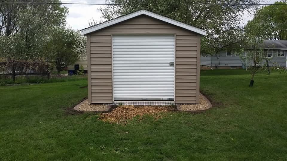 Completed storage shed — taupe siding, white roll-up door, gravel base