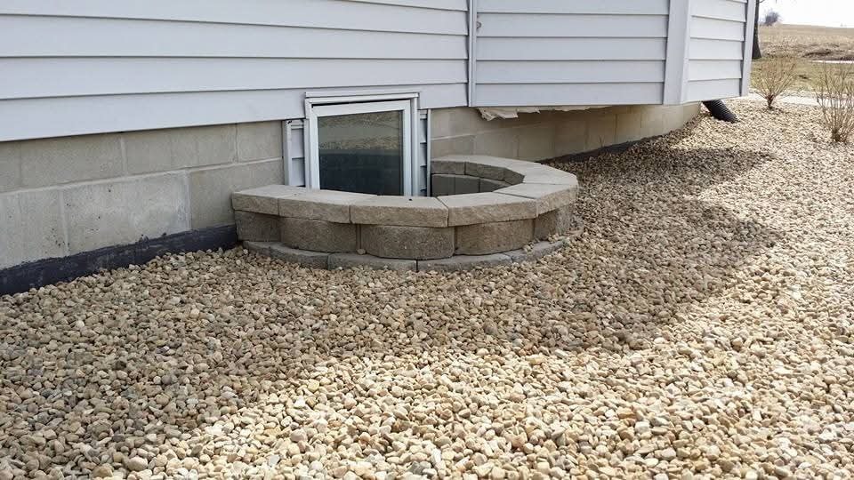 Curved block egress window well with gravel bed — side of home