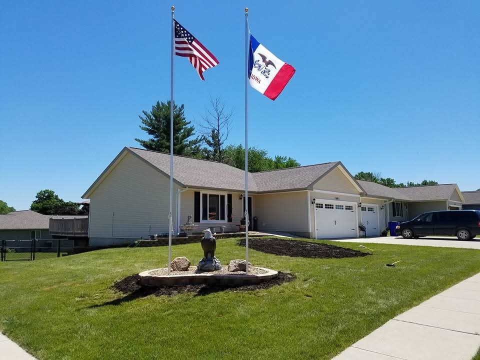 Completed ranch home exterior — US and Iowa flags, eagle statue, fresh landscaping