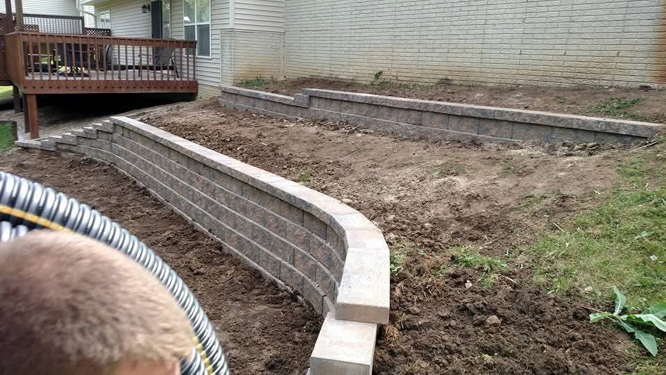 Tiered retaining wall installation in progress — backyard slope with deck