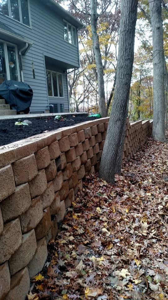 Tall block retaining wall with mulch bed — wooded backyard, fall foliage