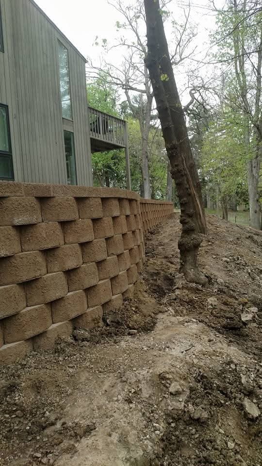 Long block retaining wall along wooded hillside — full length view