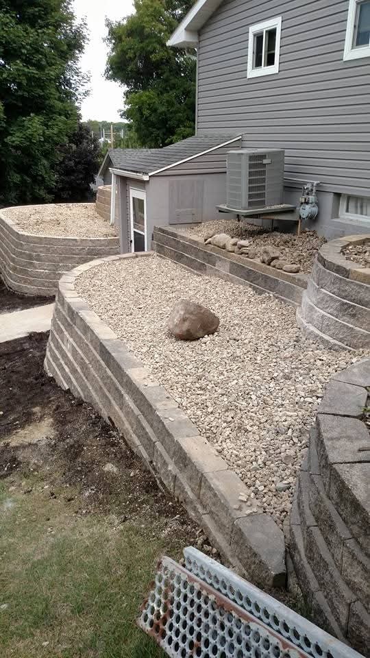 Multi-tier curved retaining walls with gravel beds — AC unit and walkout door