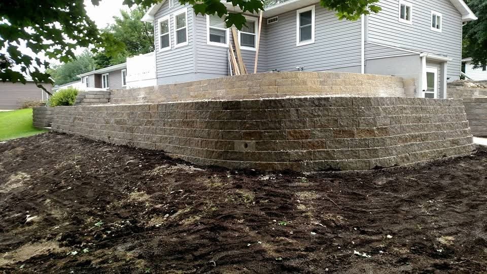 Large curved block retaining wall — freshly graded backyard, two-story home