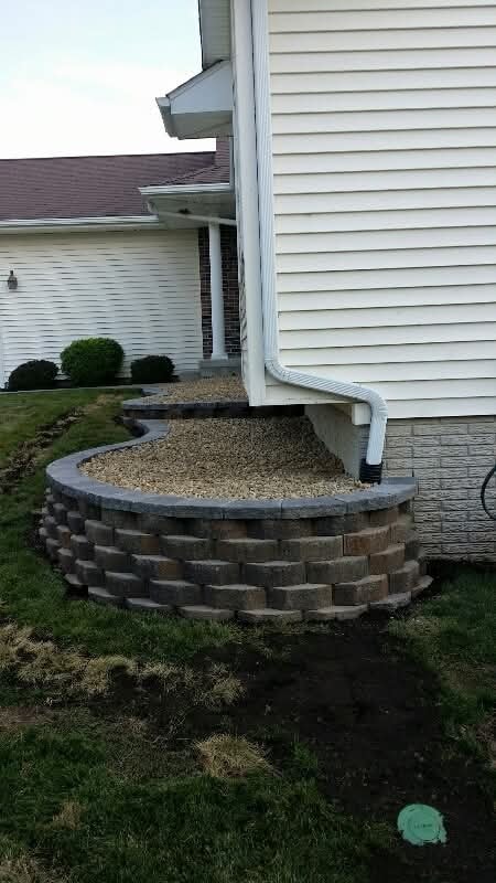 Curved block retaining wall with gravel bed — downspout drainage detail