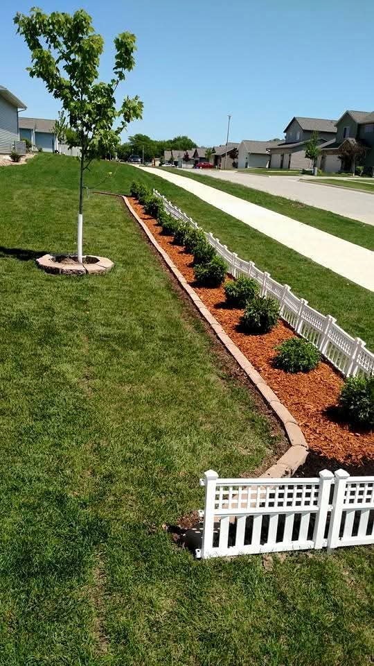 Long mulch garden bed with shrubs and white picket edging — residential street