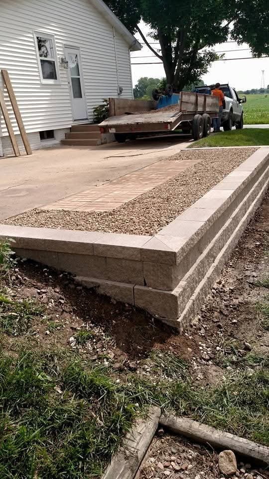 Block retaining wall and gravel bed under construction — crew and dump trailer on site