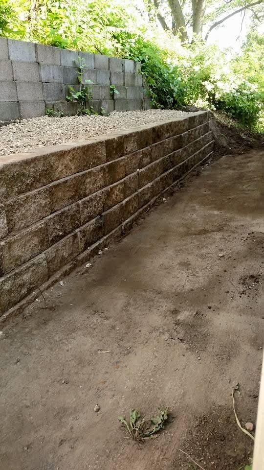 Block retaining wall with gravel backfill — wooded lot, cinder block backdrop