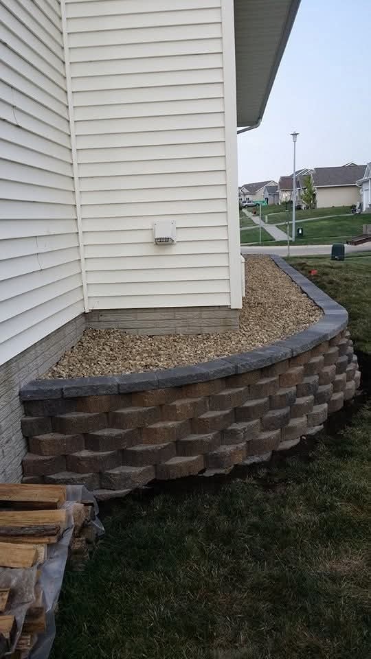 Curved block retaining wall with gravel bed — corner of white siding home